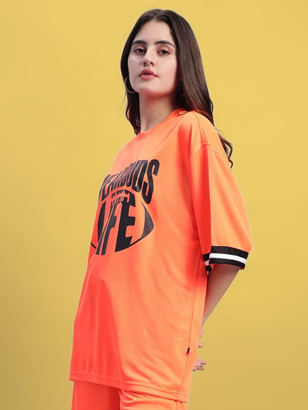Woman wearing a women's oversized orange t-shirt with black and white accents on the sleeves against a yellow background.