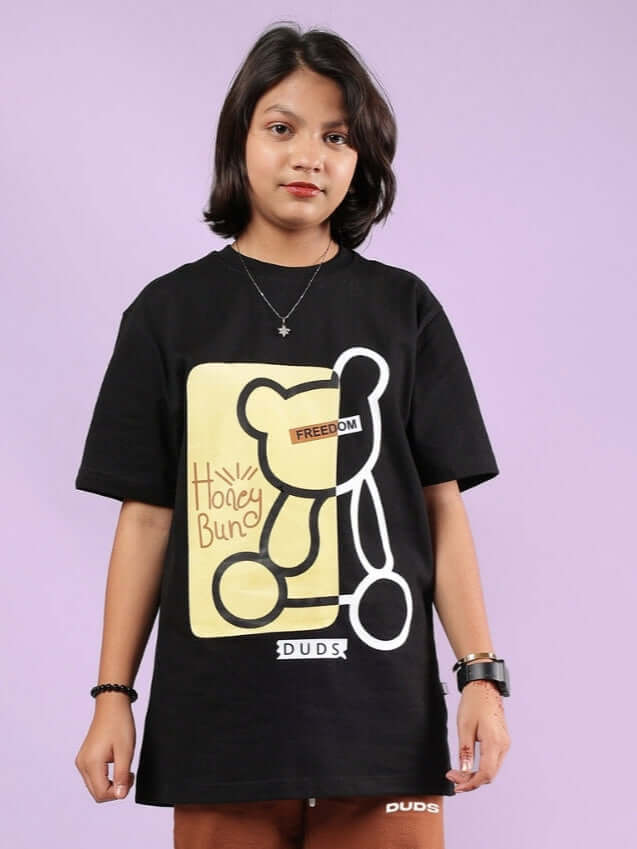 Young person wearing a black Honey-Bunny T-shirt by DUDS featuring a playful bear graphic.
