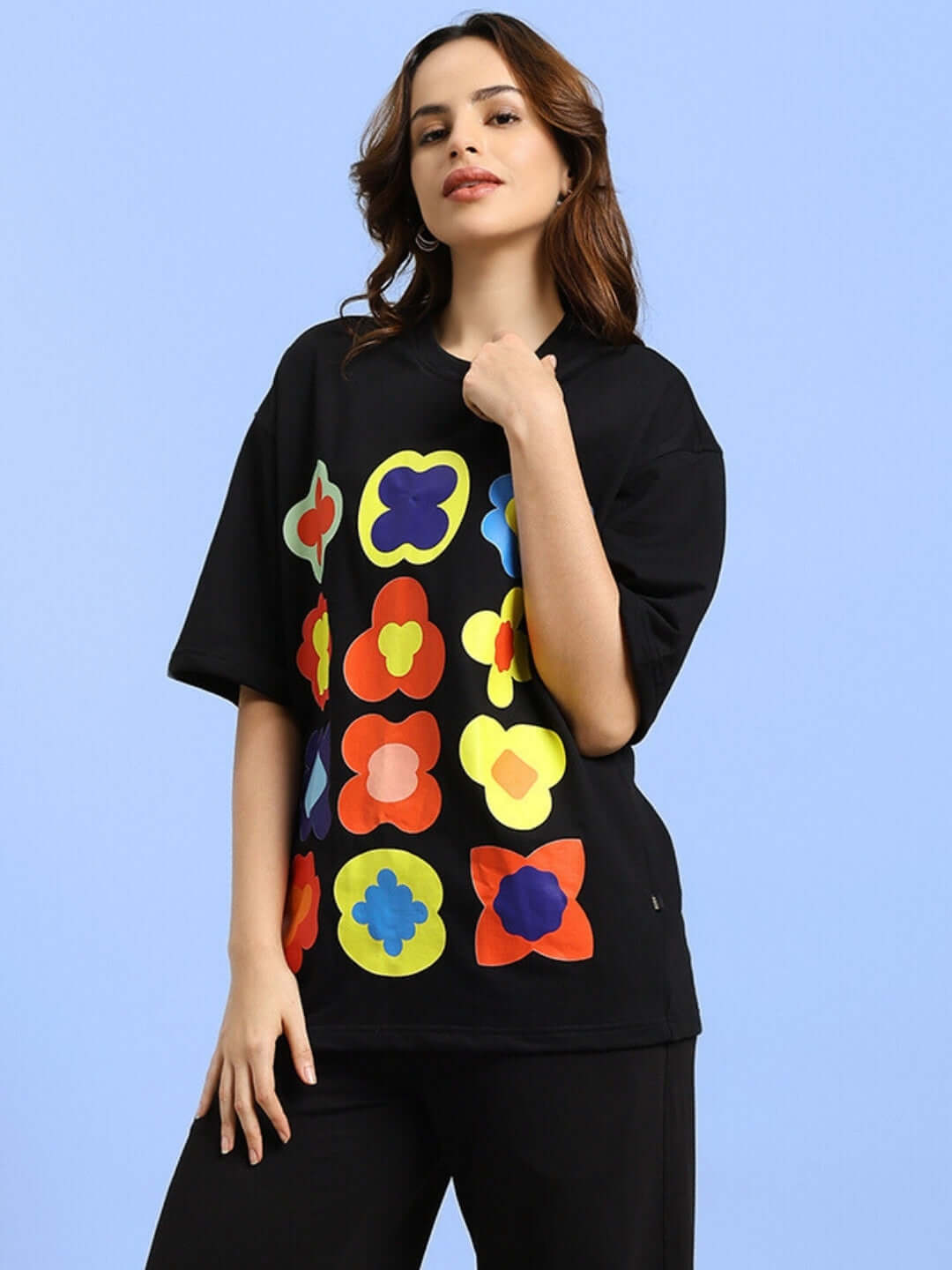 Model wearing black oversized Hollister t-shirt with colorful graphic print, made of premium cotton blend, standing against blue background.