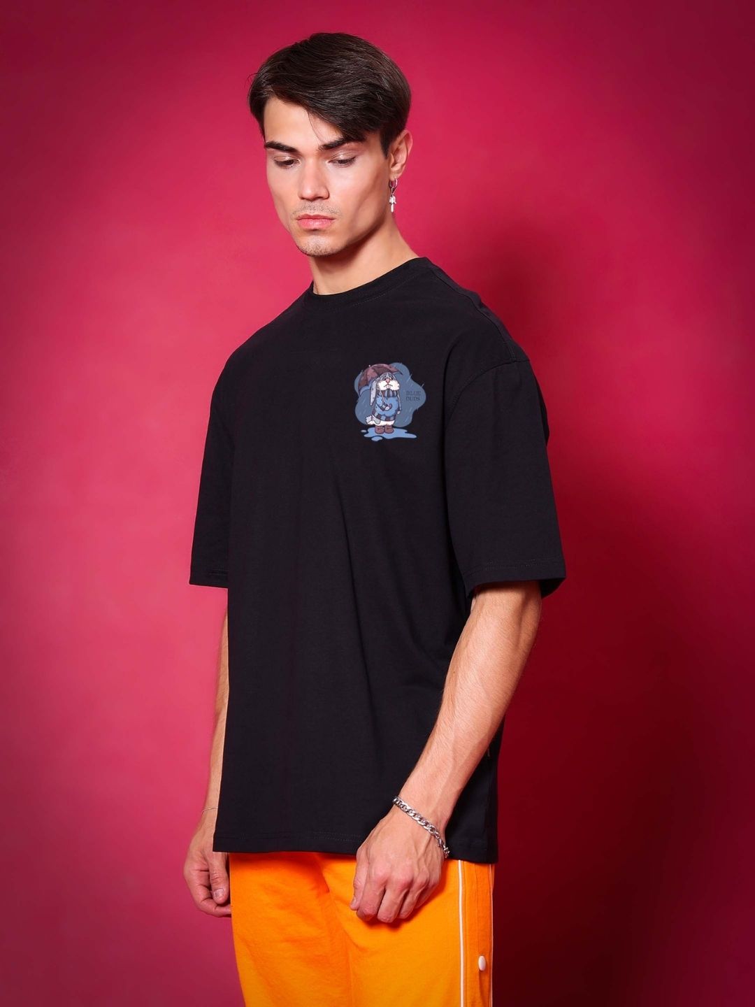Man wearing BLUE LAPIN OVER-SIZED T-SHIRT BLACK made from premium heavy gauge fabric, 97% cotton, 3% elastane, standing against red background.