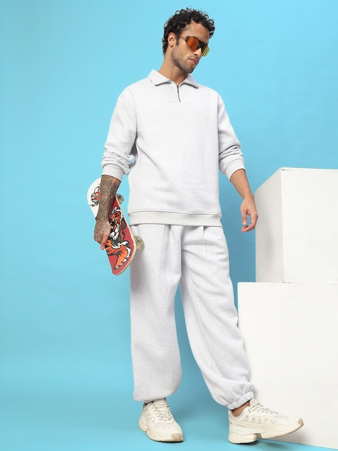 Man wearing grey fleece pants and sweatshirt with skateboard in hand, styled for casual and cozy look.