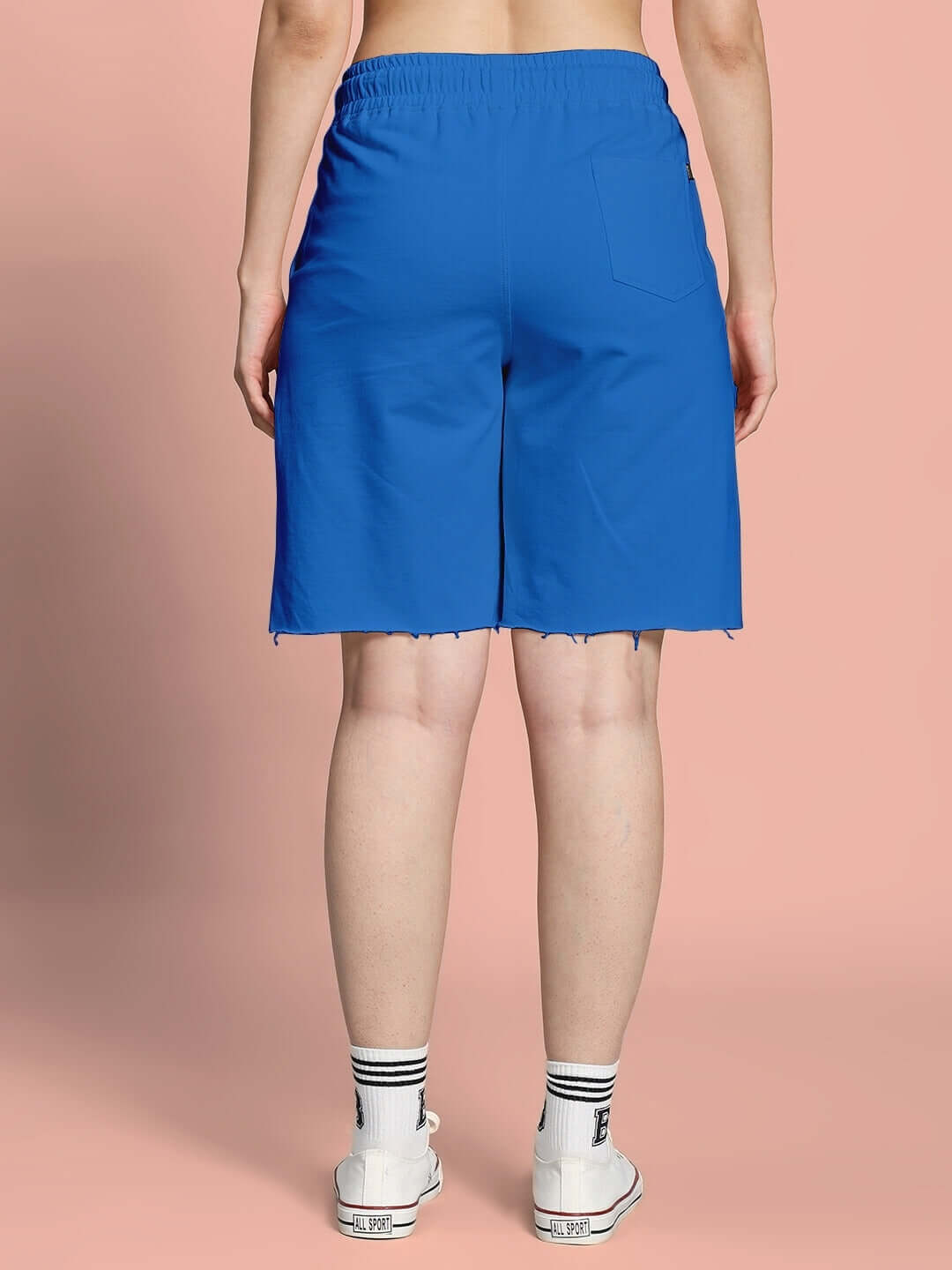 Back view of women's blue Helianthus regular fit shorts, showcasing elastic waistband and casual style against a peach background.