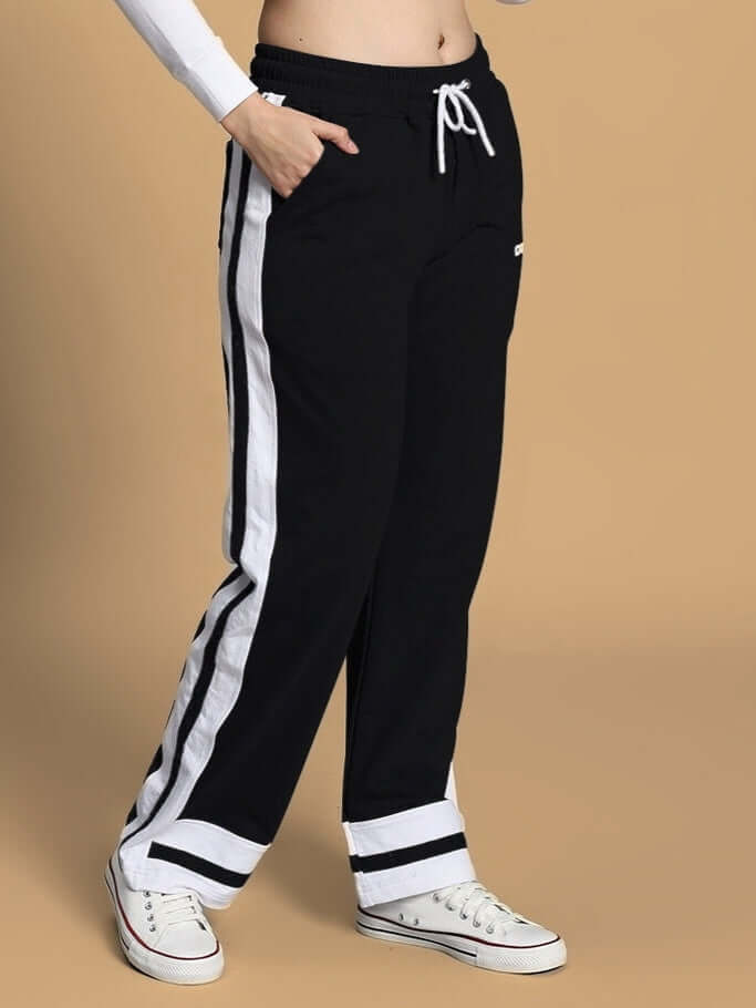 Women's black Ronny jogger with side stripe, featuring a drawstring waist and pocket detail, paired with white sneakers on beige background.