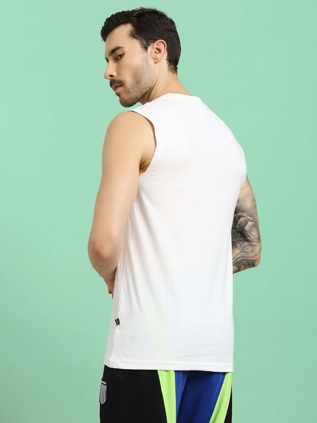 Man wearing OLIN Regular Fit Off-White T-Shirt in premium cotton fabric, showcasing back view against a green background.