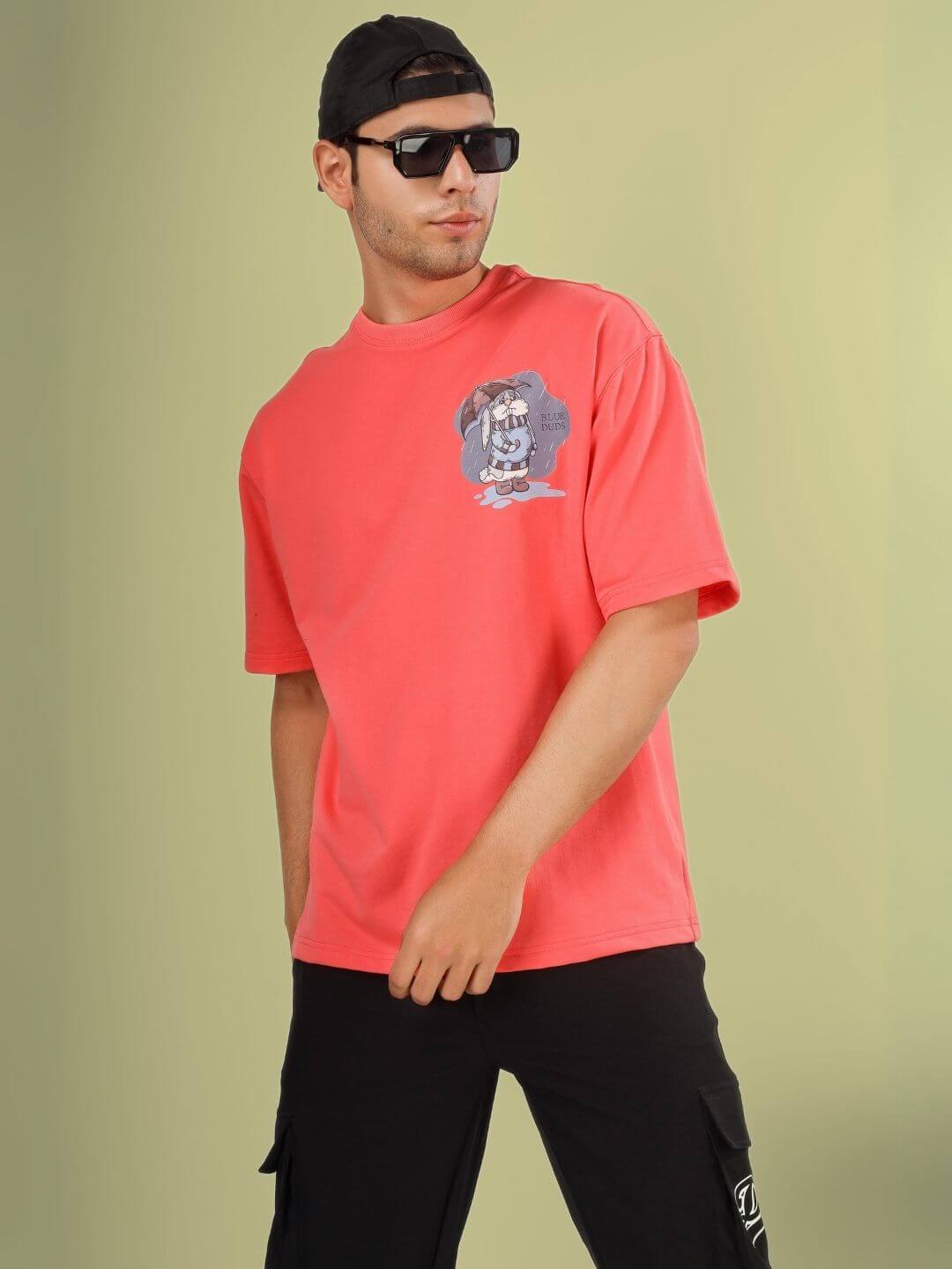 Man wearing BLUE LAPIN OVER-SIZED T-SHIRT PANTONE PEACH with graphic print, relaxed fit, posed casually against neutral background.