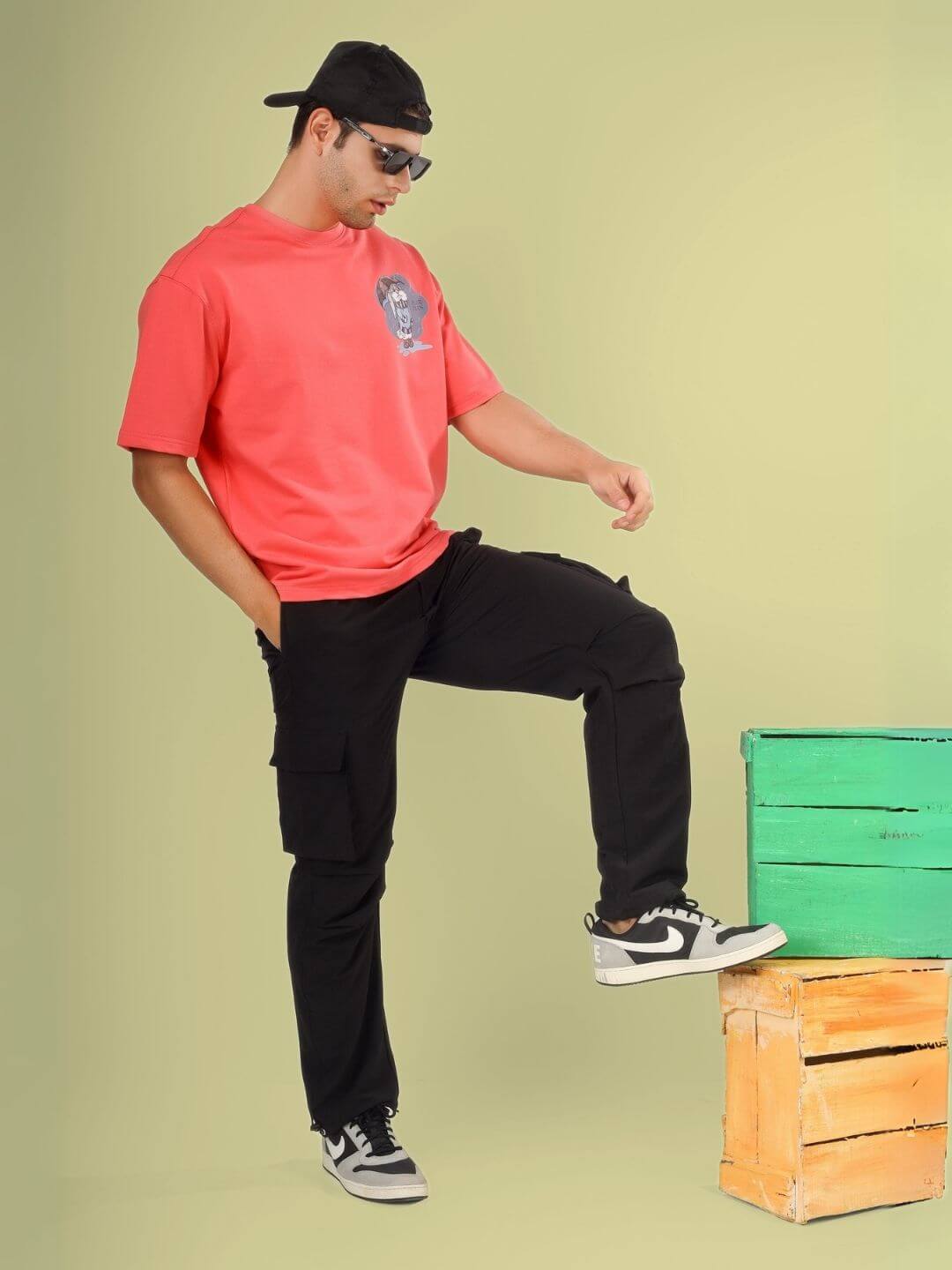 Model wearing BLUE LAPIN OVER-SIZED T-SHIRT PANTONE PEACH with black pants and sneakers, posing against a colorful backdrop.