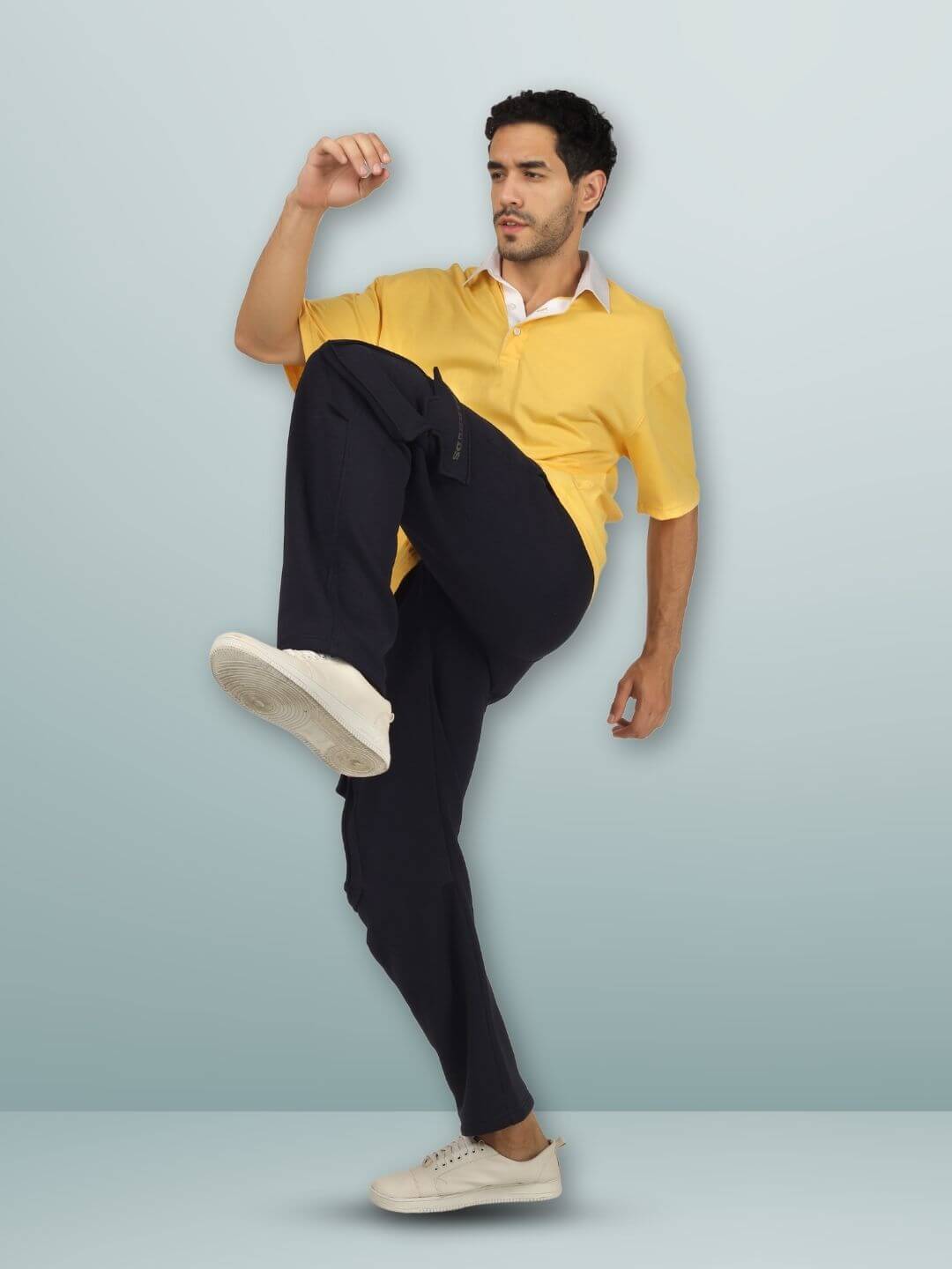 Model wearing 5 POCKET FLEECE SOLID CARGO PANT NAVY BLUE paired with yellow shirt and white sneakers, striking a dynamic pose.
