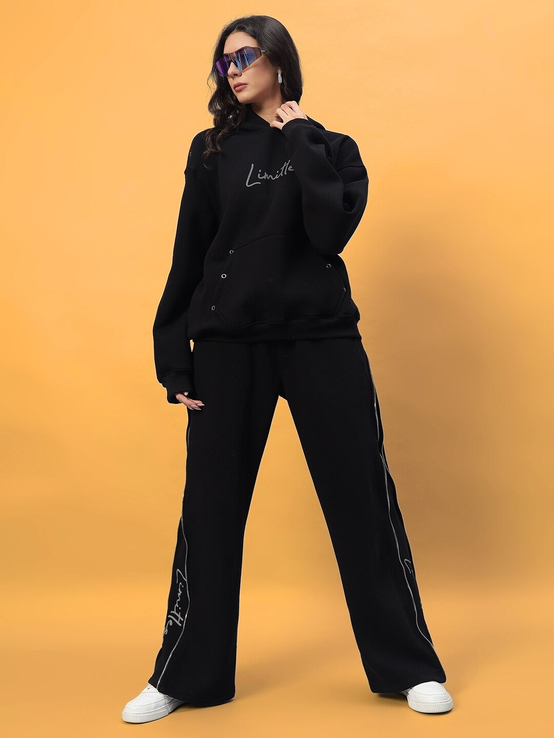 Woman wearing Women's Limitless Fleece Reflector Jogger in black, styled with matching top and white sneakers, on a yellow background.