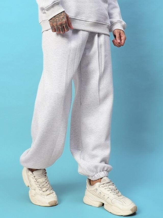 Man wearing Bona-Fide Fleece Pant in Melange Grey with sneakers on a blue background, showcasing comfort and style.