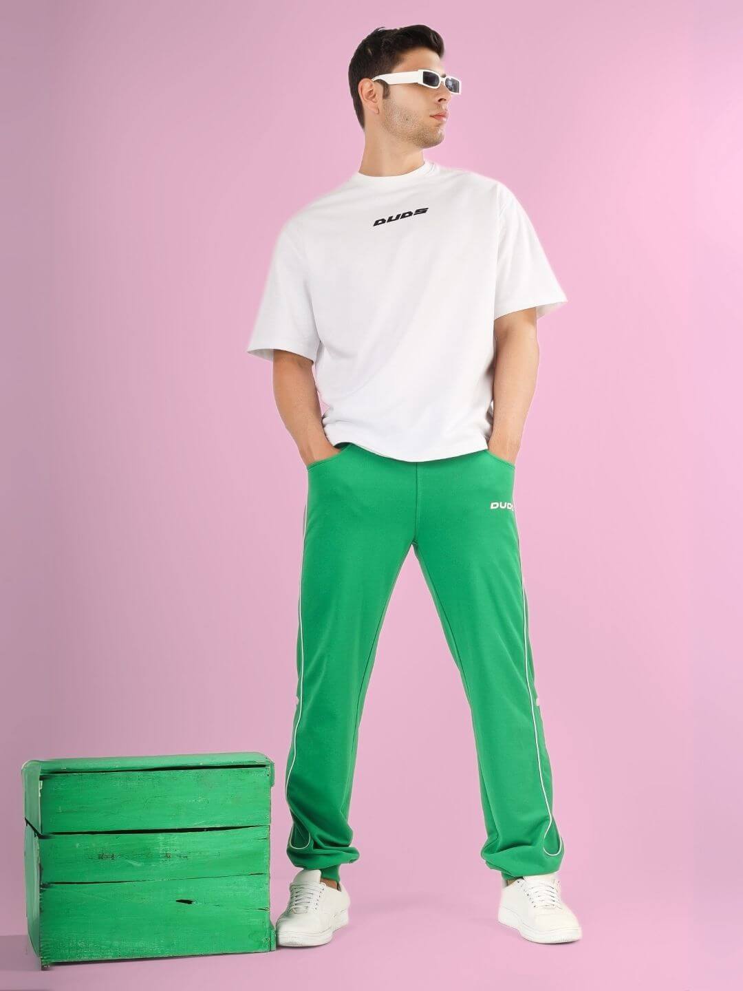 Man wearing DONT STOP OVER-SIZED T-SHIRT WHITE with green pants, standing against a pink background.