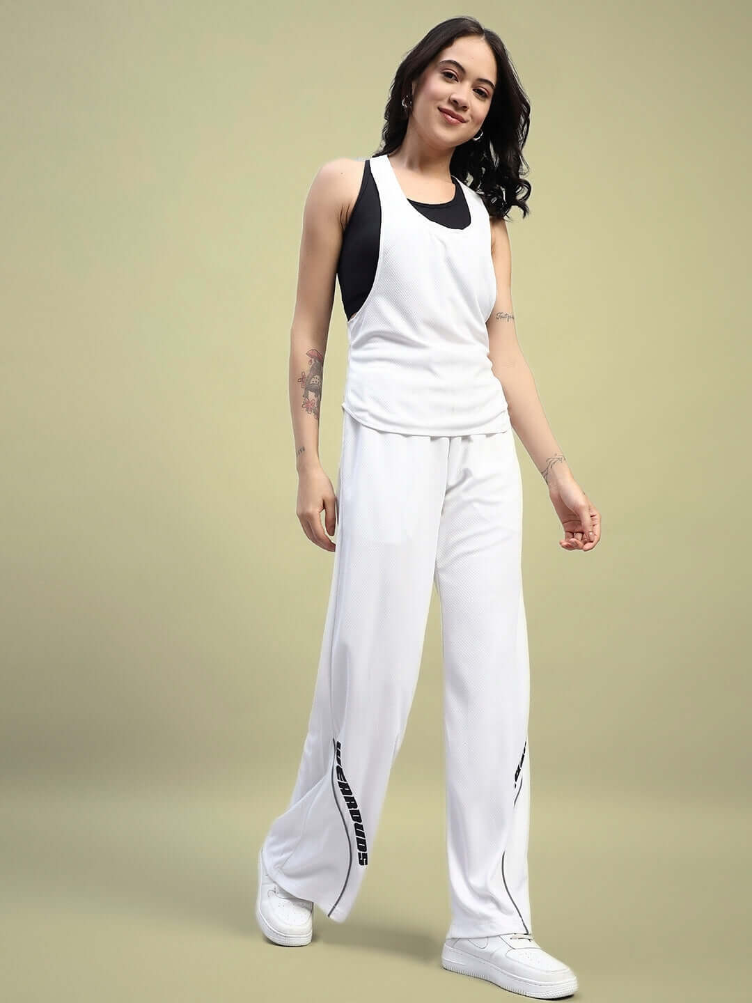 Woman wearing a white Women's Cubby Co-ord Set with relaxed fit joggers and tank top, showcasing premium sports polyester fabric.