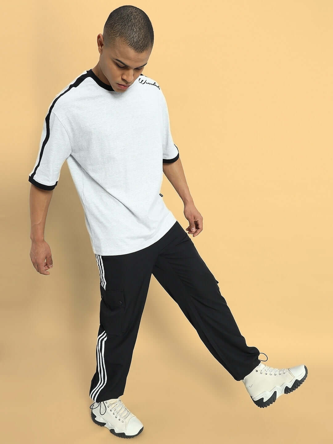 Man wearing NOVA relaxed fit black cargo pants with sporty shoes and white t-shirt in a casual style pose.