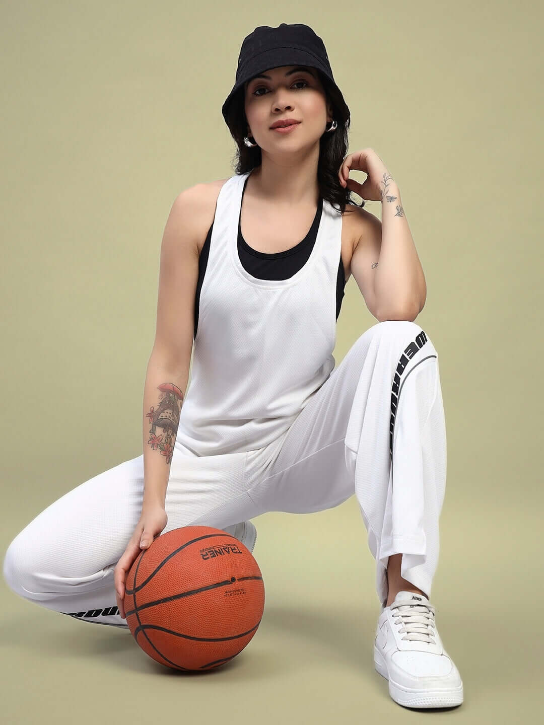 Woman in white jogger co-ord set and black hat holding basketball, showcasing relaxed fit sporty style.