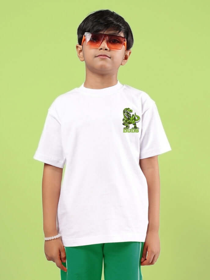 Boy wearing white ROBO REX oversized t-shirt with dinosaur print, styled with sunglasses, on a light green background.
