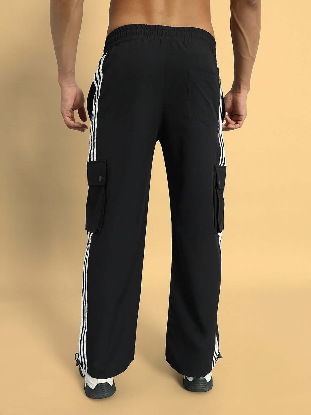 Back view of black NOVA Relaxed Fit Cargo Pants with side stripes on a beige background.