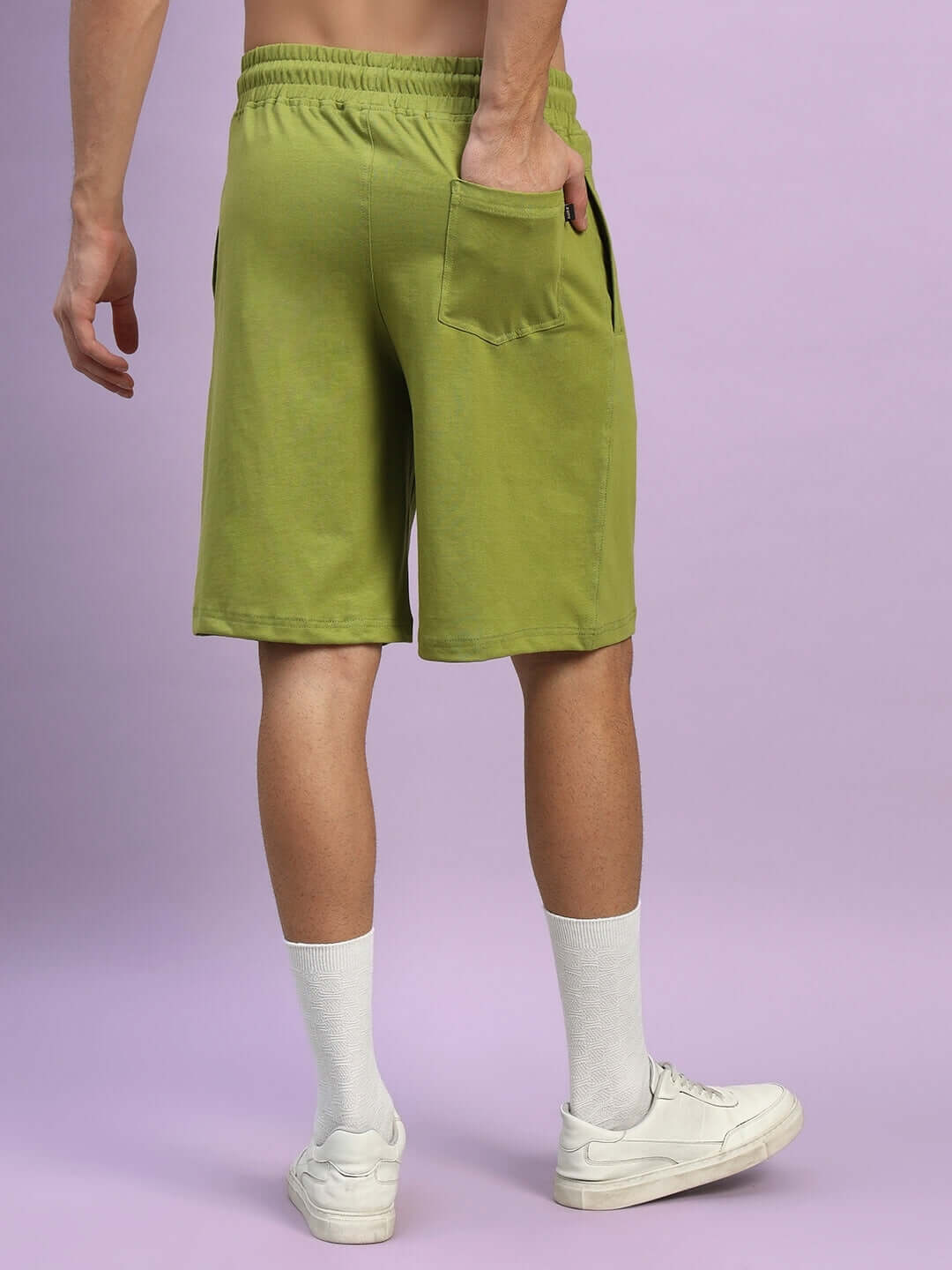 Back view of olive green wideline regular fit shorts with pocket detail, paired with white socks and sneakers on a purple background.
