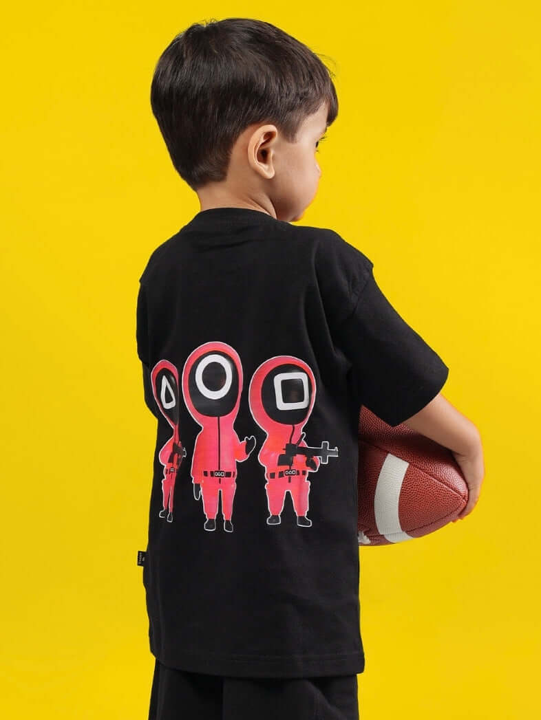 Child wearing black Squid Battle T-shirt with cartoon figures, holding a football, yellow background.