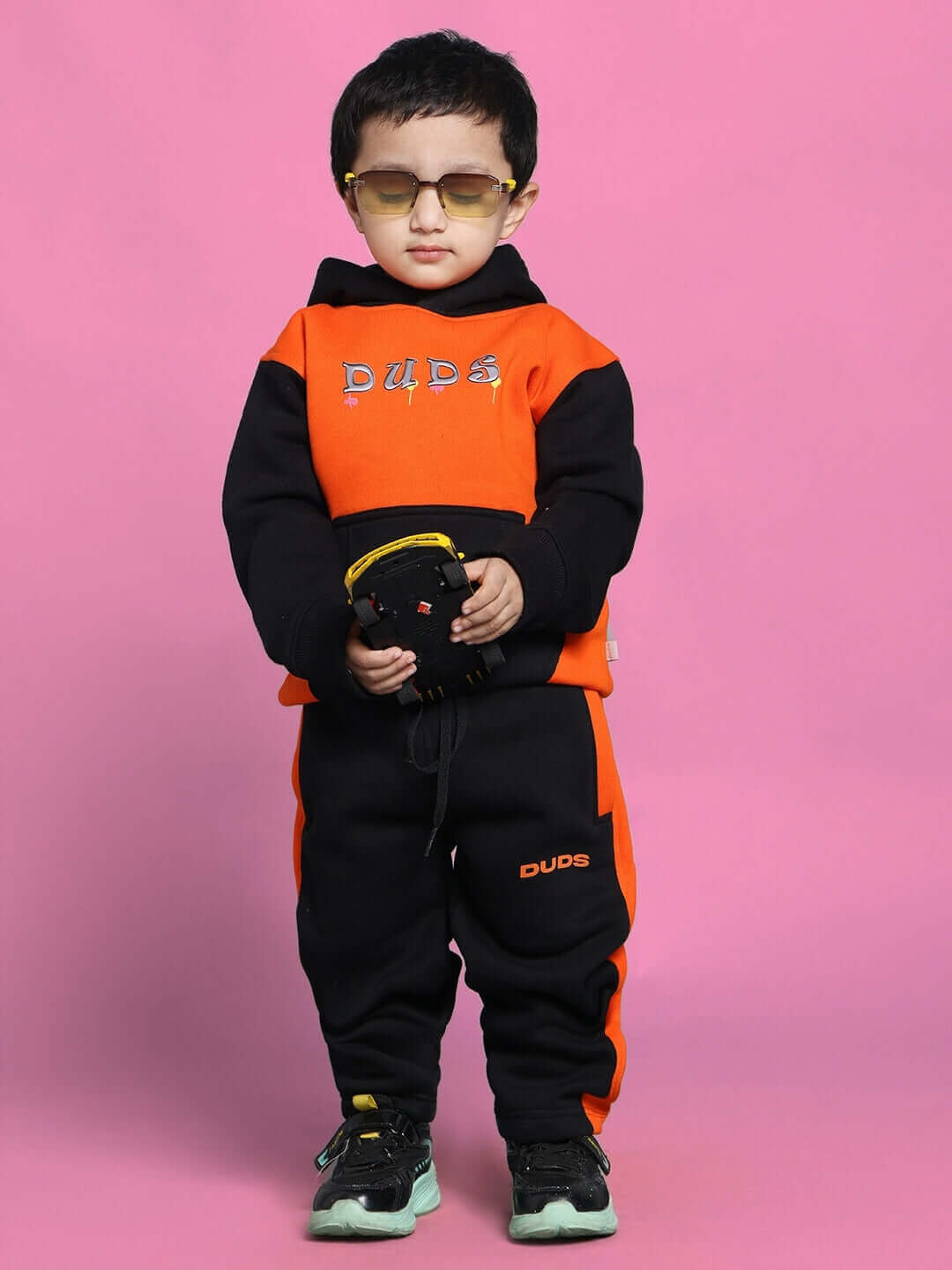 Child wearing black-orange COOL TEDDY co-ord set for boys and girls with sunglasses against a pink background.