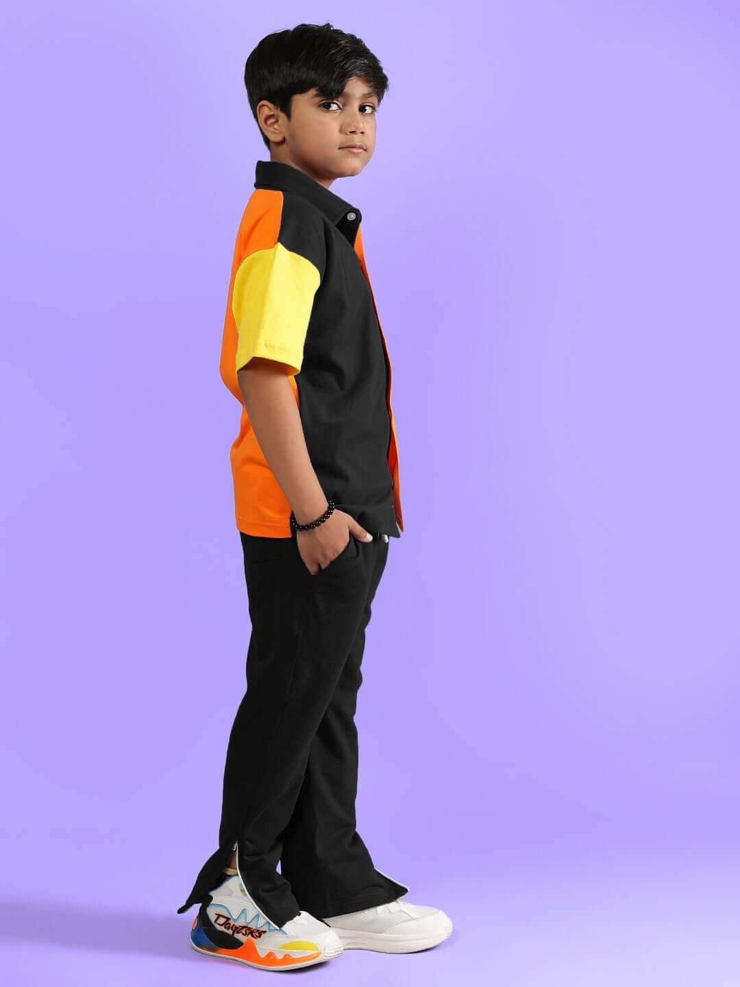 Child wearing Apex Co-Ord set in multi-black with orange and yellow accents, standing sideways on purple background.
