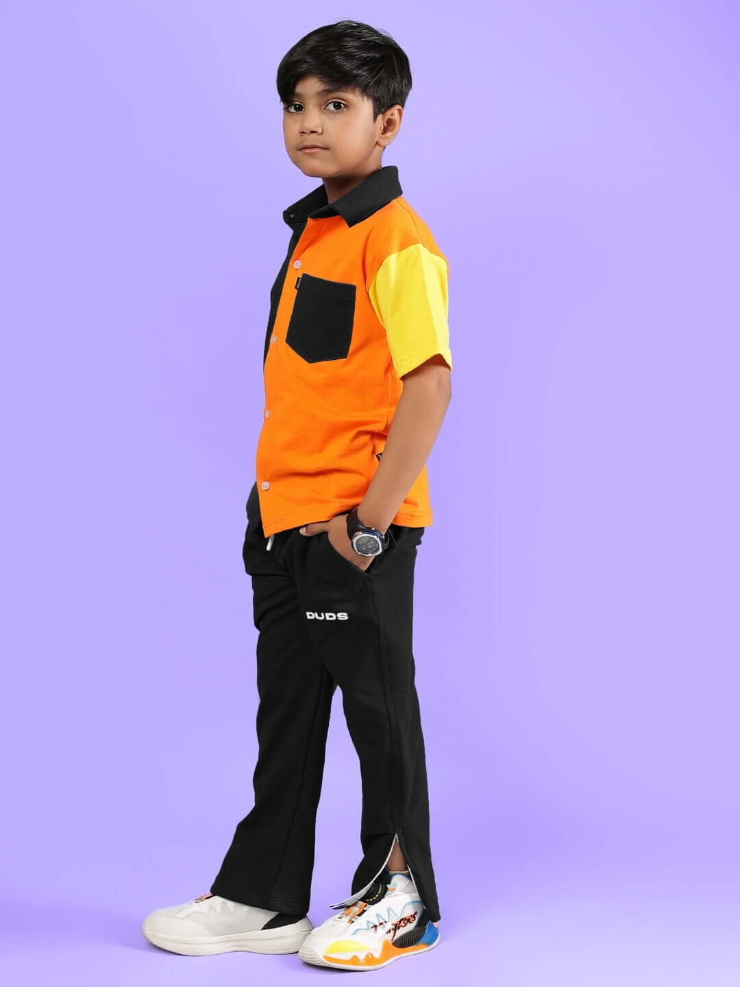 A young boy wearing APEX Co-Ord in multi-black by DUDS, featuring orange and black shirt with matching pants, stands confidently.
