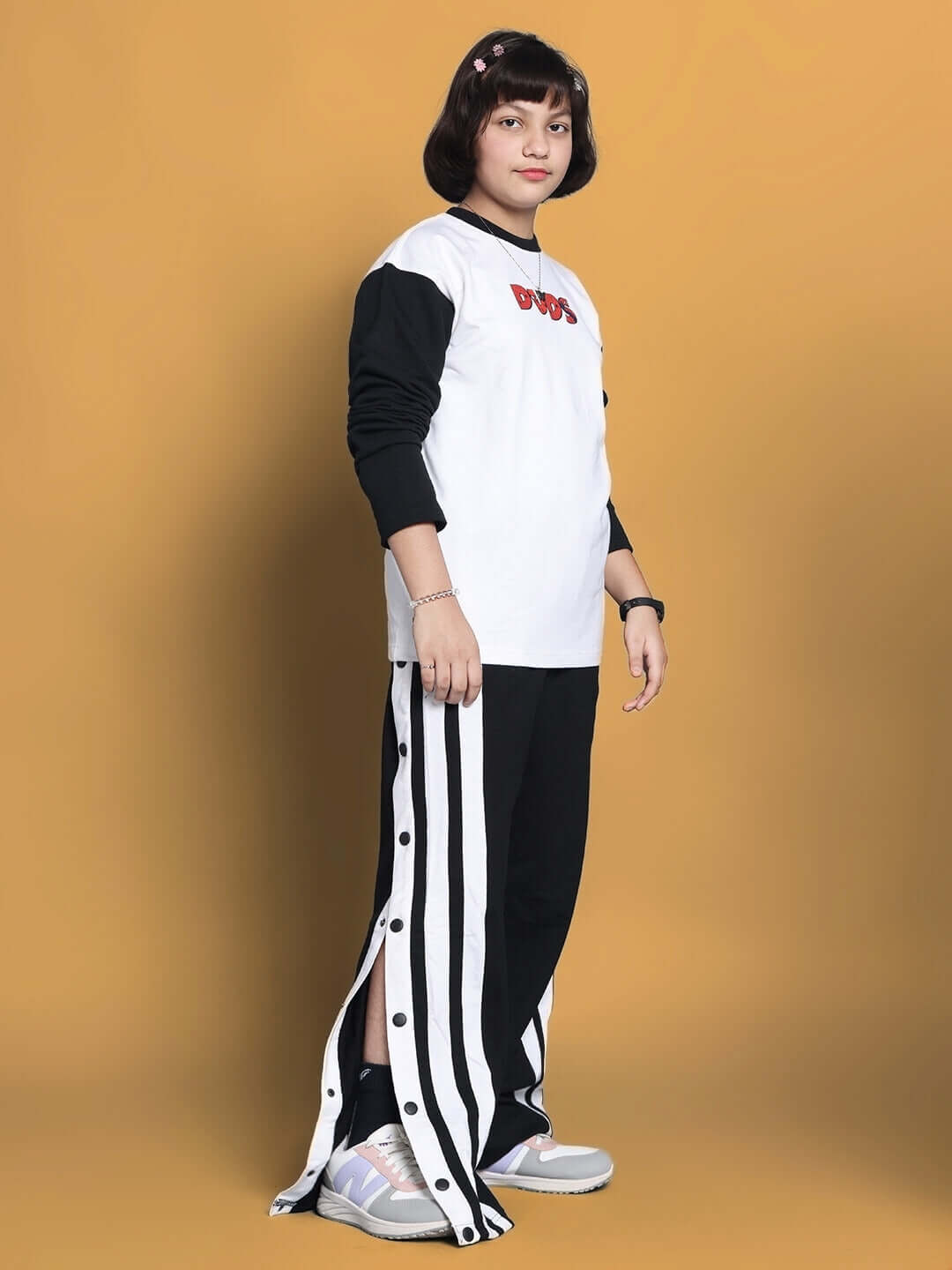 Child wearing a black and white BITSY co-ord set with side-striped pants against a yellow background.