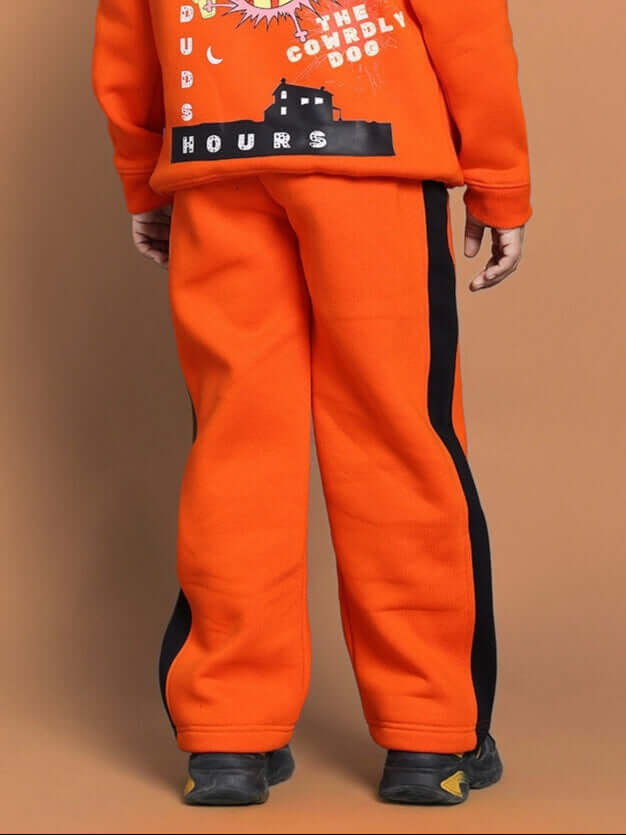 Child wearing orange Courage fleece pants with black stripes, viewed from the back, standing against a brown background.