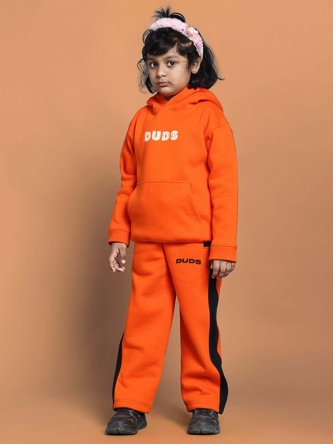 Child wearing orange COURAGE CO-ORD set for boys and girls, featuring hoodie and pants with black accents, set against orange background.