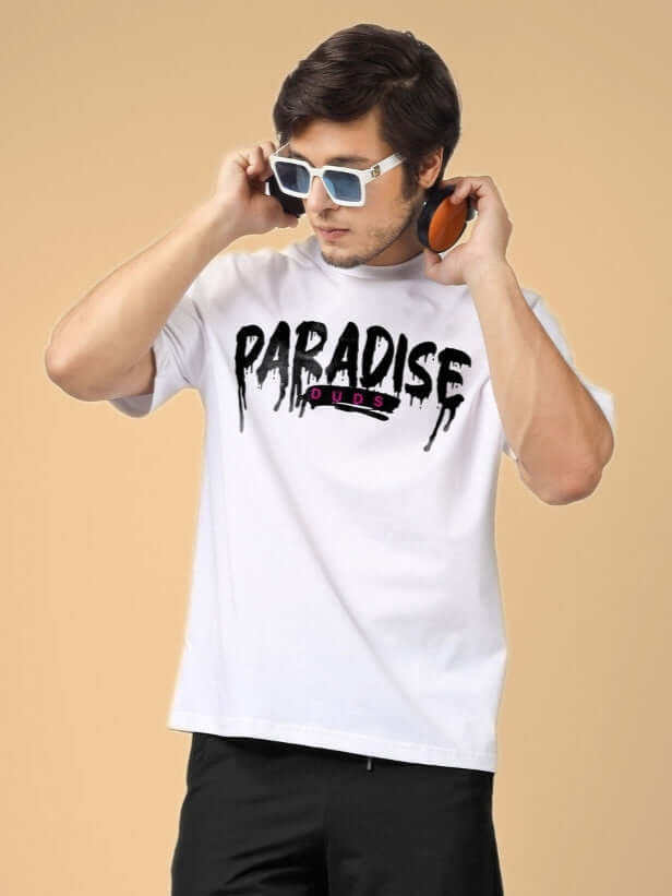 Man wearing white Paradise oversized t-shirt, sunglasses, and headphones, showcasing a trendy summer fashion look.