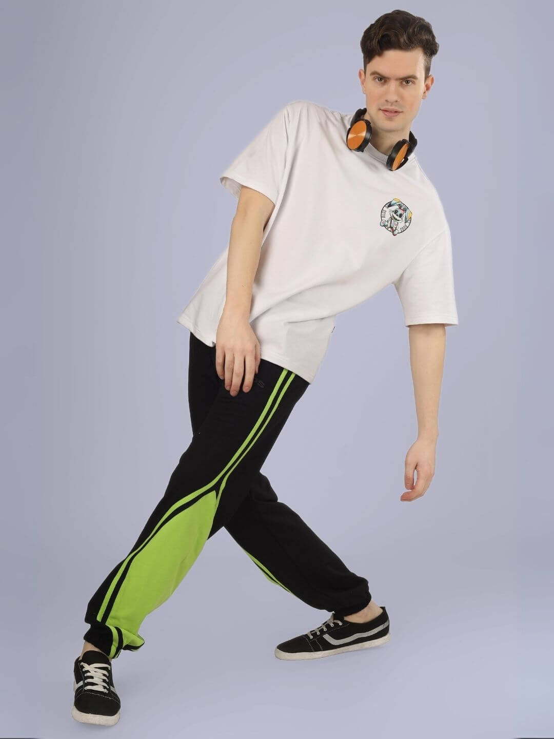 Model wearing A Doll Not Rabbit oversized printed t-shirt in white, paired with black and green pants, leaning casually with headphones.
