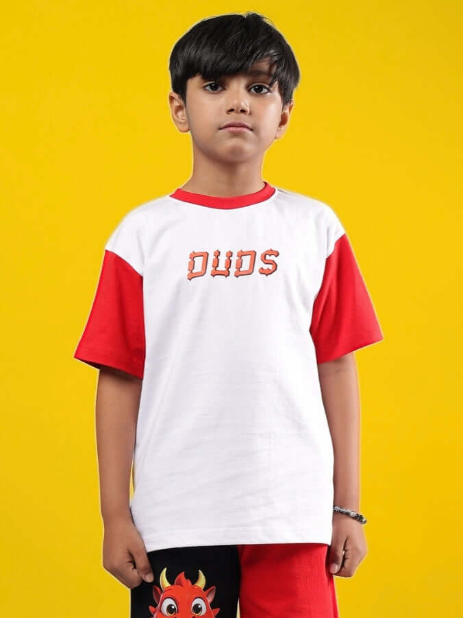 Child wearing CASSIE T-Shirt for Boys & Girls, white with red sleeves, featuring DUDS logo, standing against a yellow background.