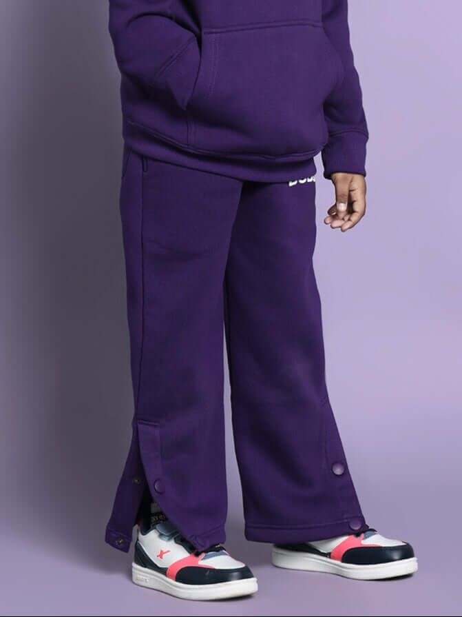 Child wearing purple miller co-ord set for boys and girls with sneakers standing against a purple background.