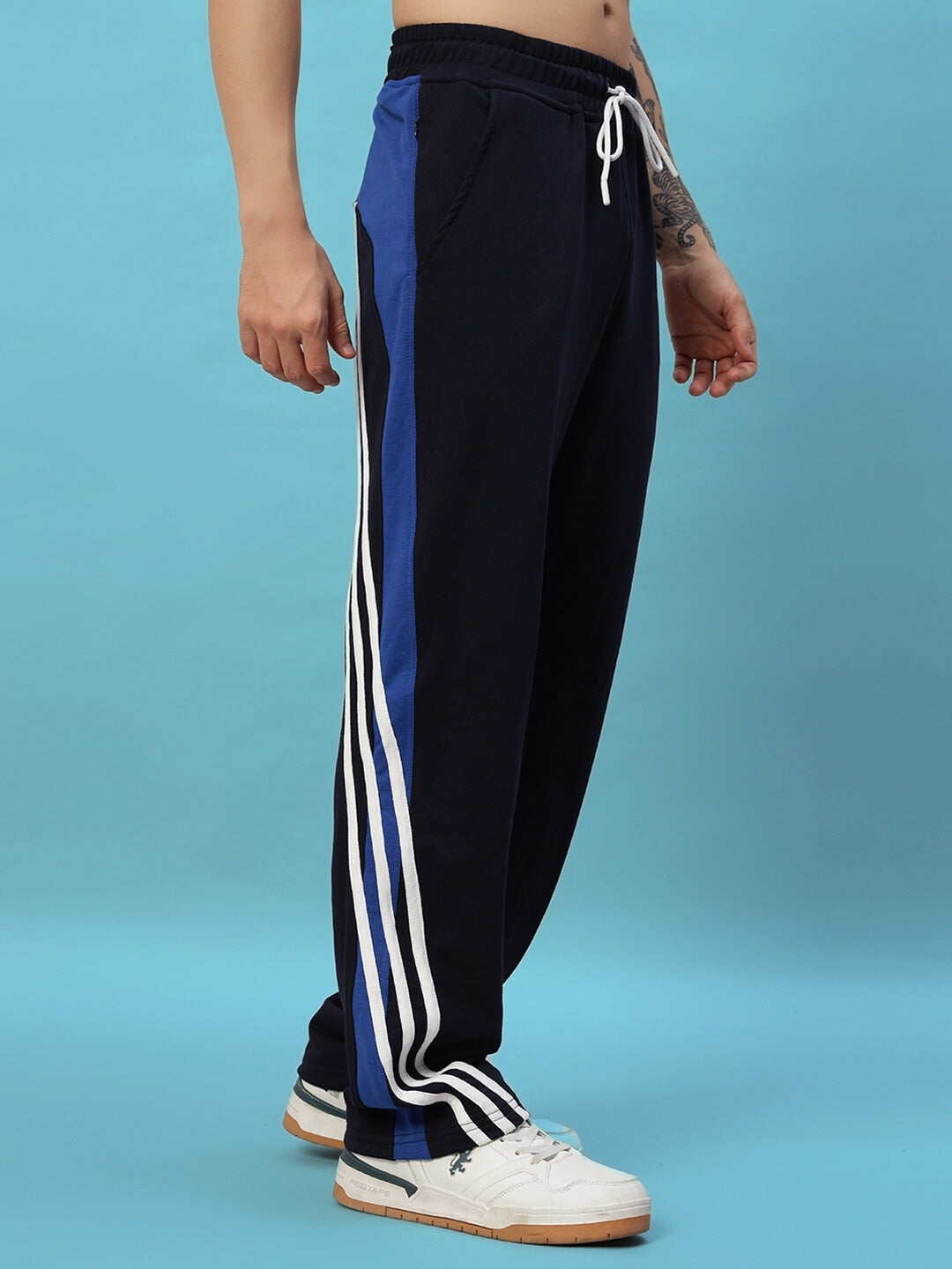 Navy blue Tangle relaxed-fit joggers with white and blue stripes, modeled against a blue background.