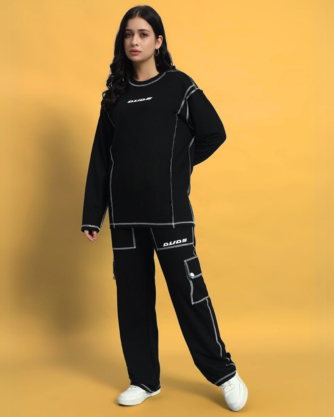 Woman wearing black WOMEN'S DYNAMIC 5 POCKET CARGO PANT by DUDS, standing against yellow background.