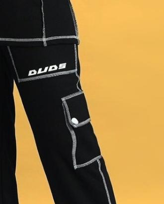 Black women's dynamic cargo pant with five pockets, contrast stitching, and DUDS logo, showcasing detailed craftsmanship against yellow background.