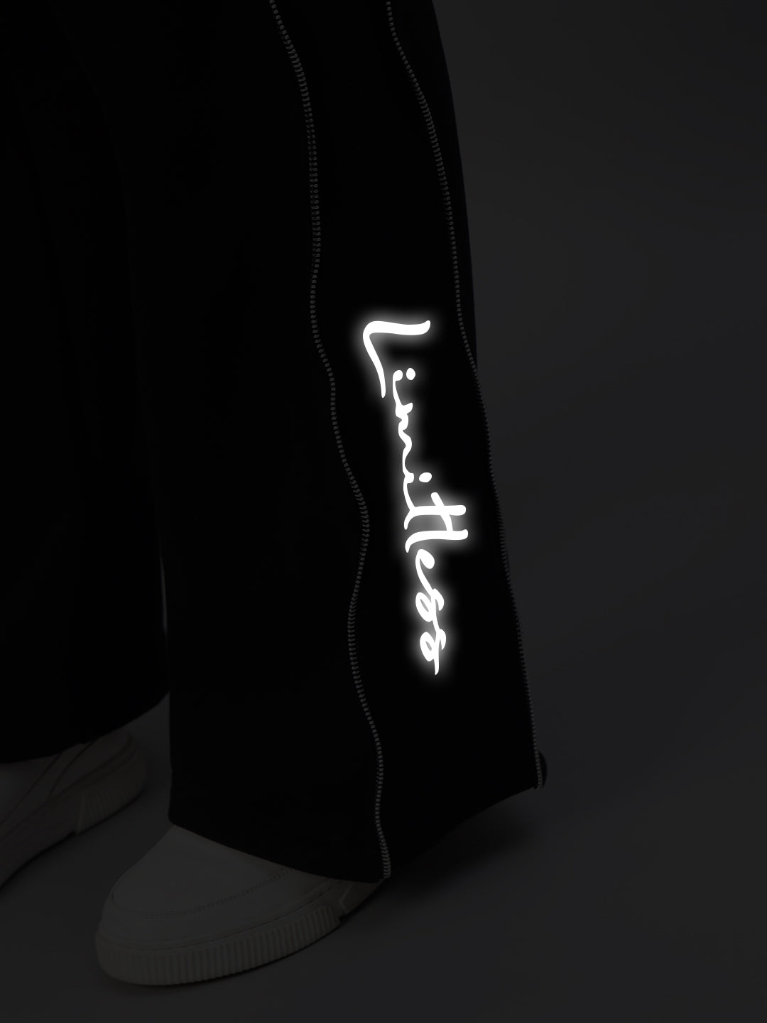 Close-up of Women's Limitless Fleece Reflector Jogger in Black, showcasing reflective 'Limitless' text and white stitching detail.