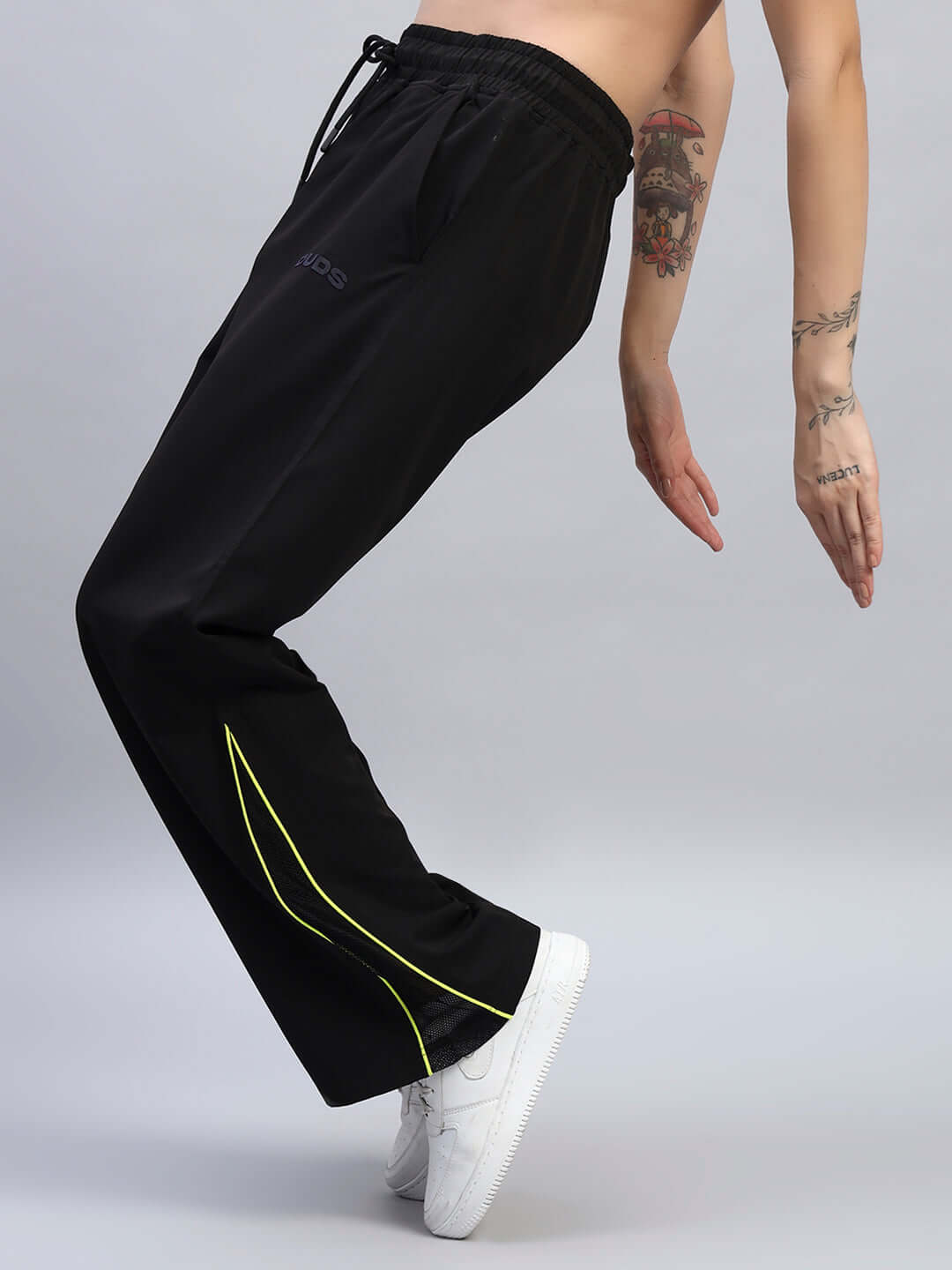 Person wearing black relaxed-fit joggers with yellow accents, demonstrating flexibility and fit, ankle showing, studio setting.
