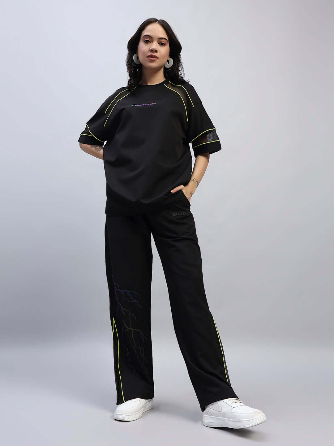 Woman wearing black Women's Salvo Reflector Co-Ord Set, made of premium sports polyester fabric, with reflective details, hands in pockets.