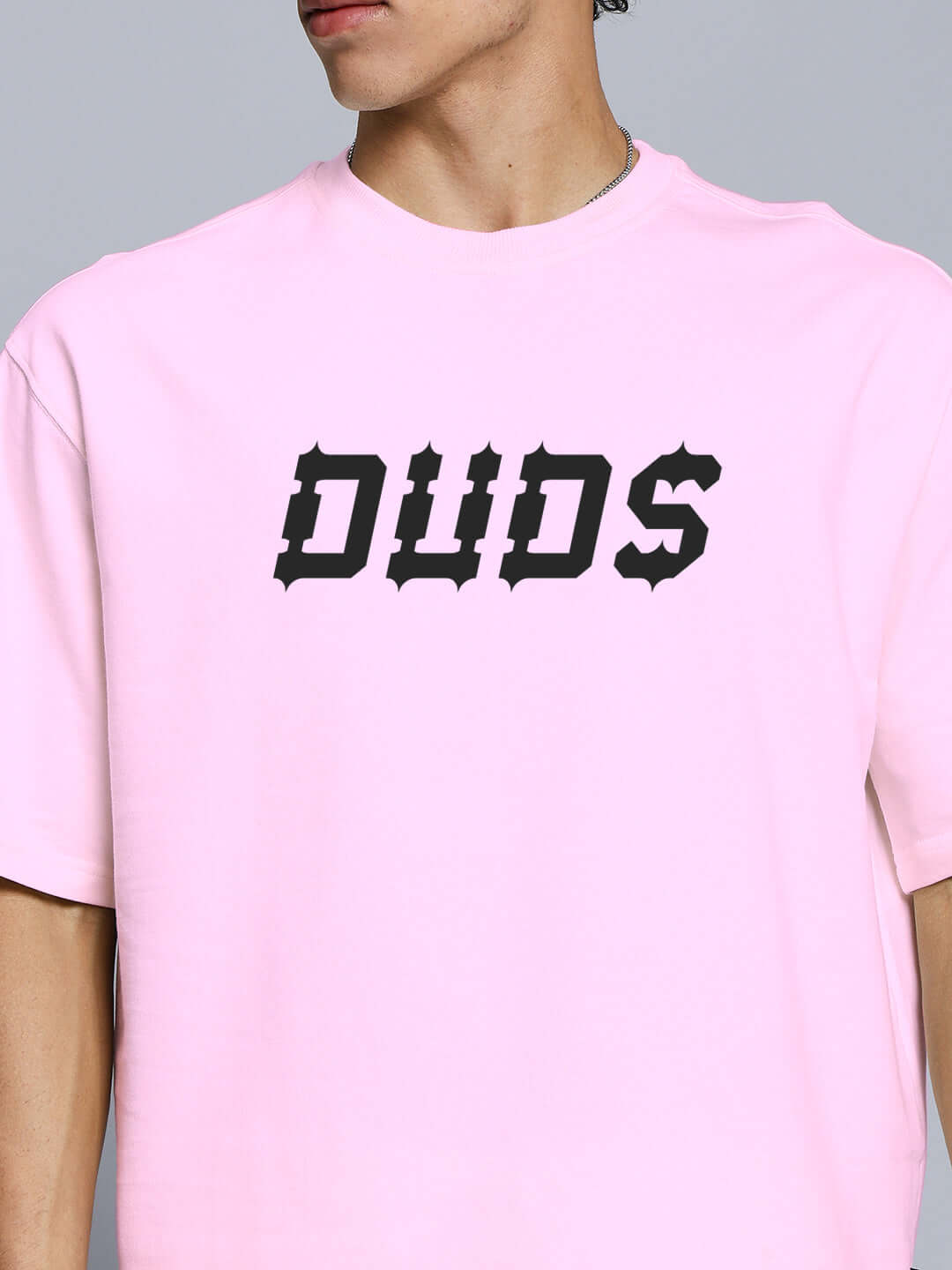 Close-up of a person wearing a pink T-shirt with 'DUDS' printed in stylized black font on the front.
