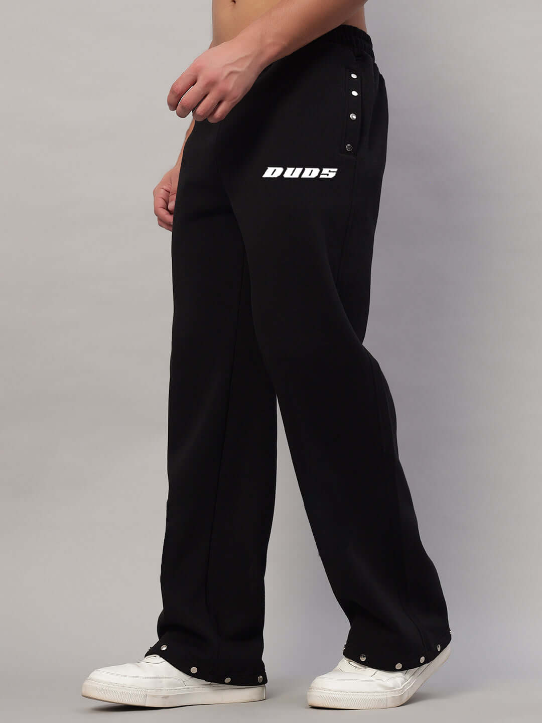 Model wearing black rigid cotton fleece jogger pants with white text detail, side view, paired with white sneakers.