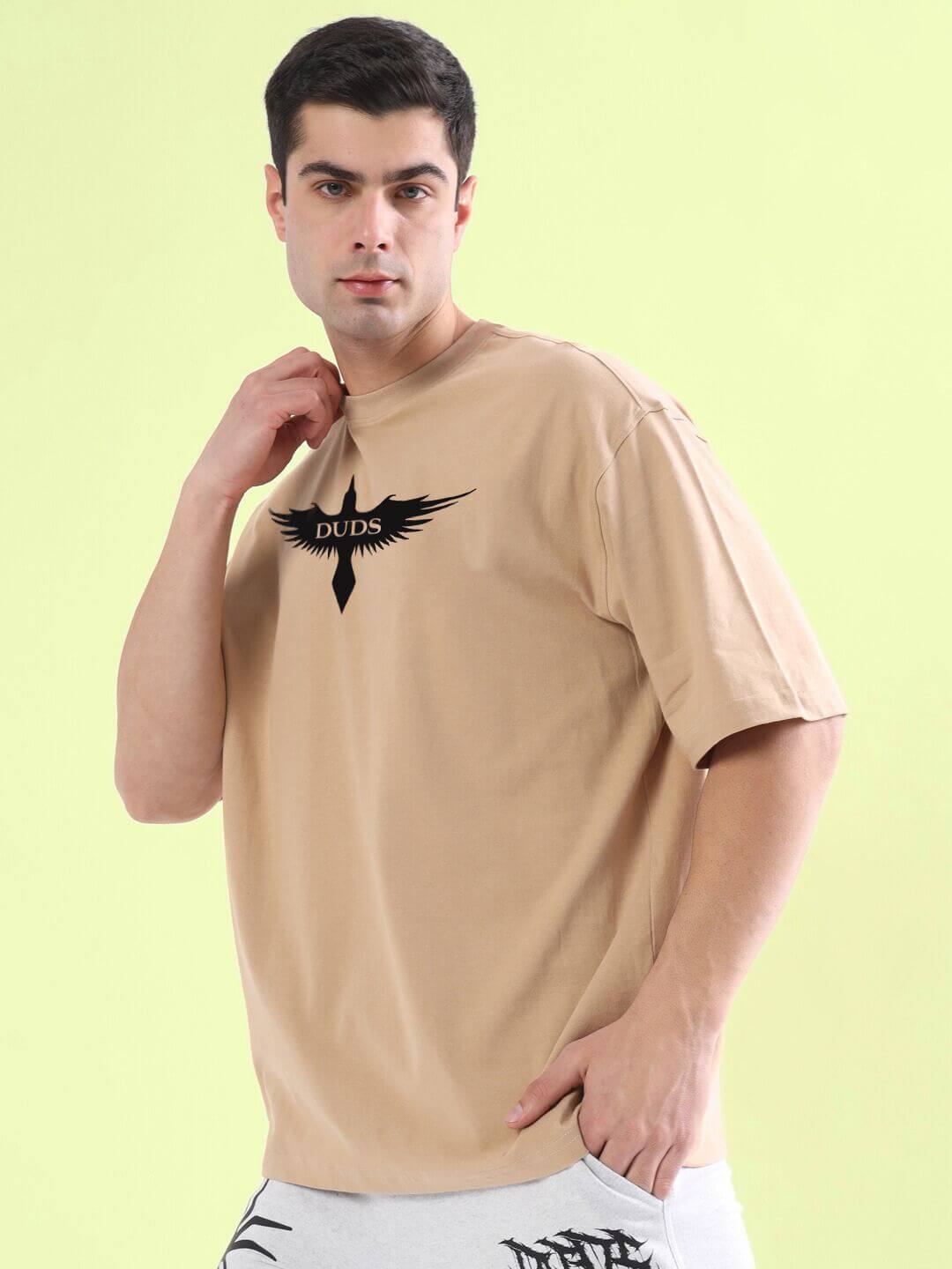 Man wearing SILENT BUT POWERFUL PRINTED T-SHIRT BEIGE with black graphic design, standing against a light green background.