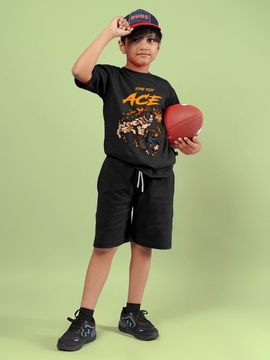 Child wearing ACE co-ord set in black, holding a football, standing against a green background. Unisex fashion for boys and girls.