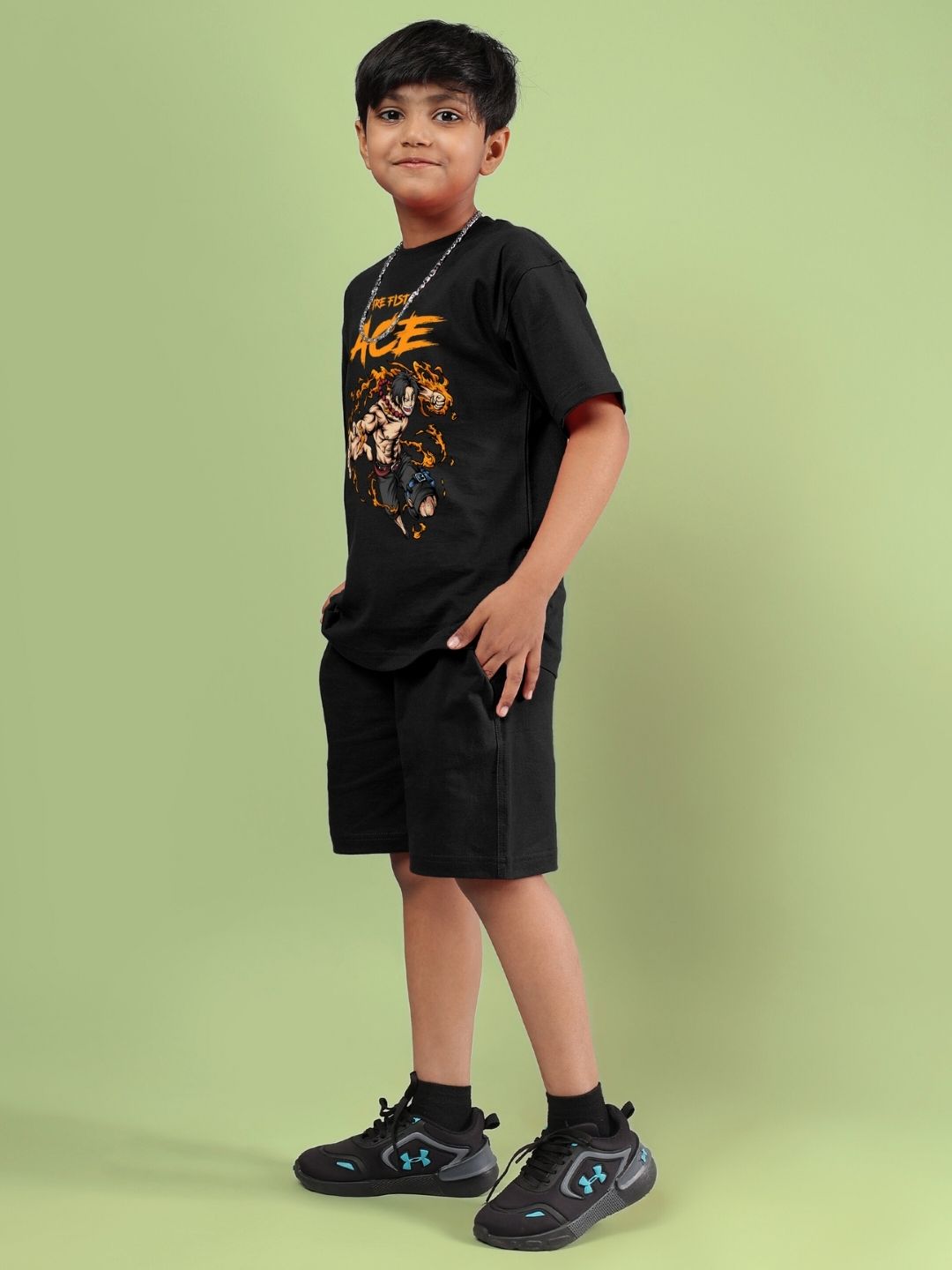 Child wearing ACE co-ord set for boys and girls in black, featuring a printed top and comfortable shorts, standing against a green background.