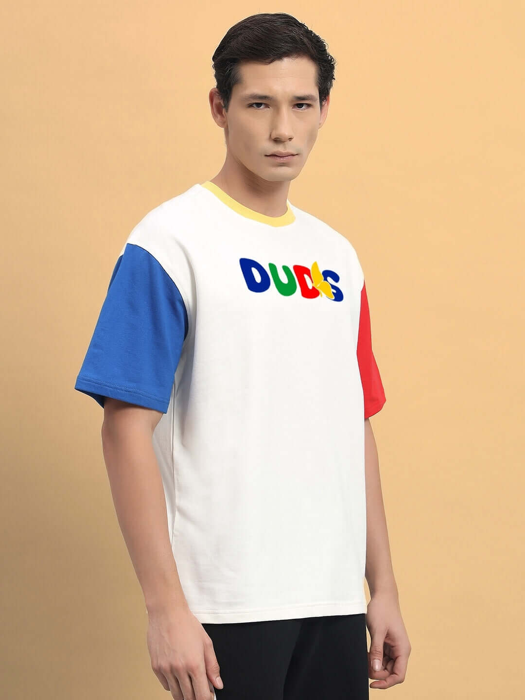Model wearing Adonis color blocked oversized T-shirt, off white, with red, blue sleeves and vibrant logo design, made in India.