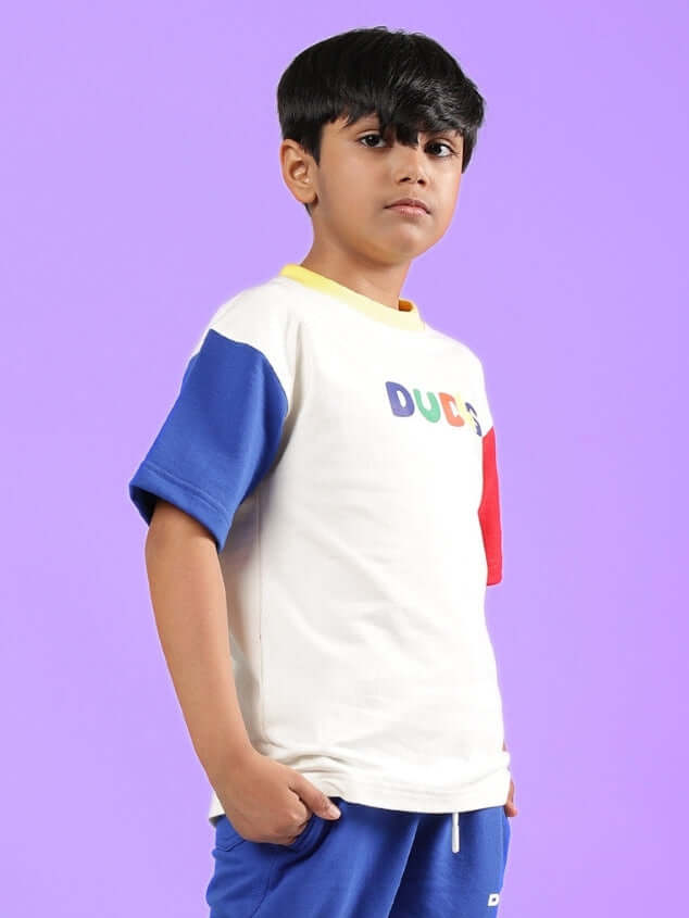Young boy wearing ADONIS oversized off-white T-shirt for boys & girls, featuring blue and red sleeves, by DUDS.