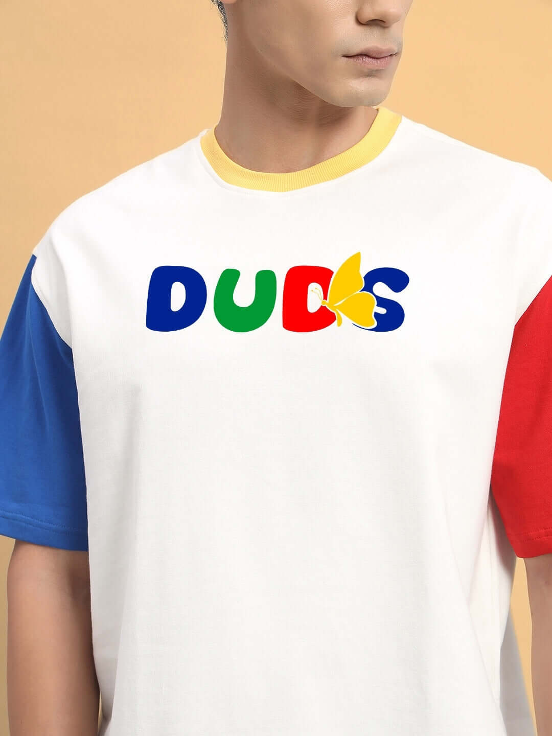 Man wearing color-blocked oversized t-shirt with 'DUDS' logo in red, blue, and green on white fabric, featuring blue and red sleeves.