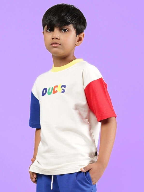 Child wearing ADONIS oversized off-white t-shirt with colorful sleeves and DUDS logo, perfect for boys and girls, on purple background.