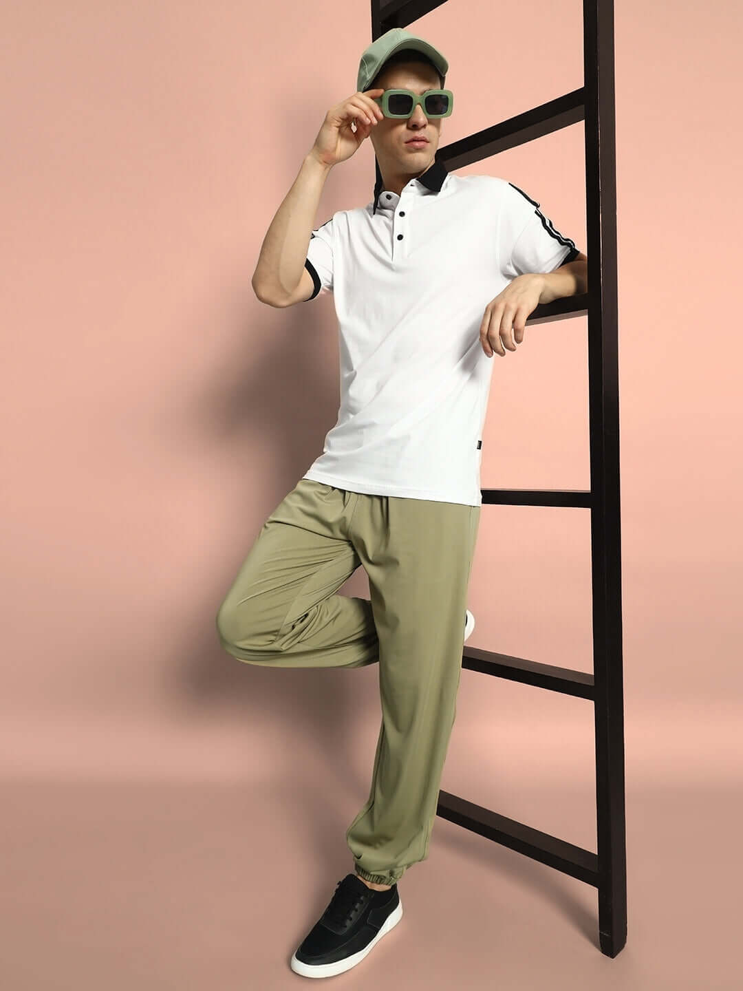 Model wearing AGILE RELAXED PANT JOGGER in olive green, paired with a white polo shirt and sneakers, leaning on a ladder.