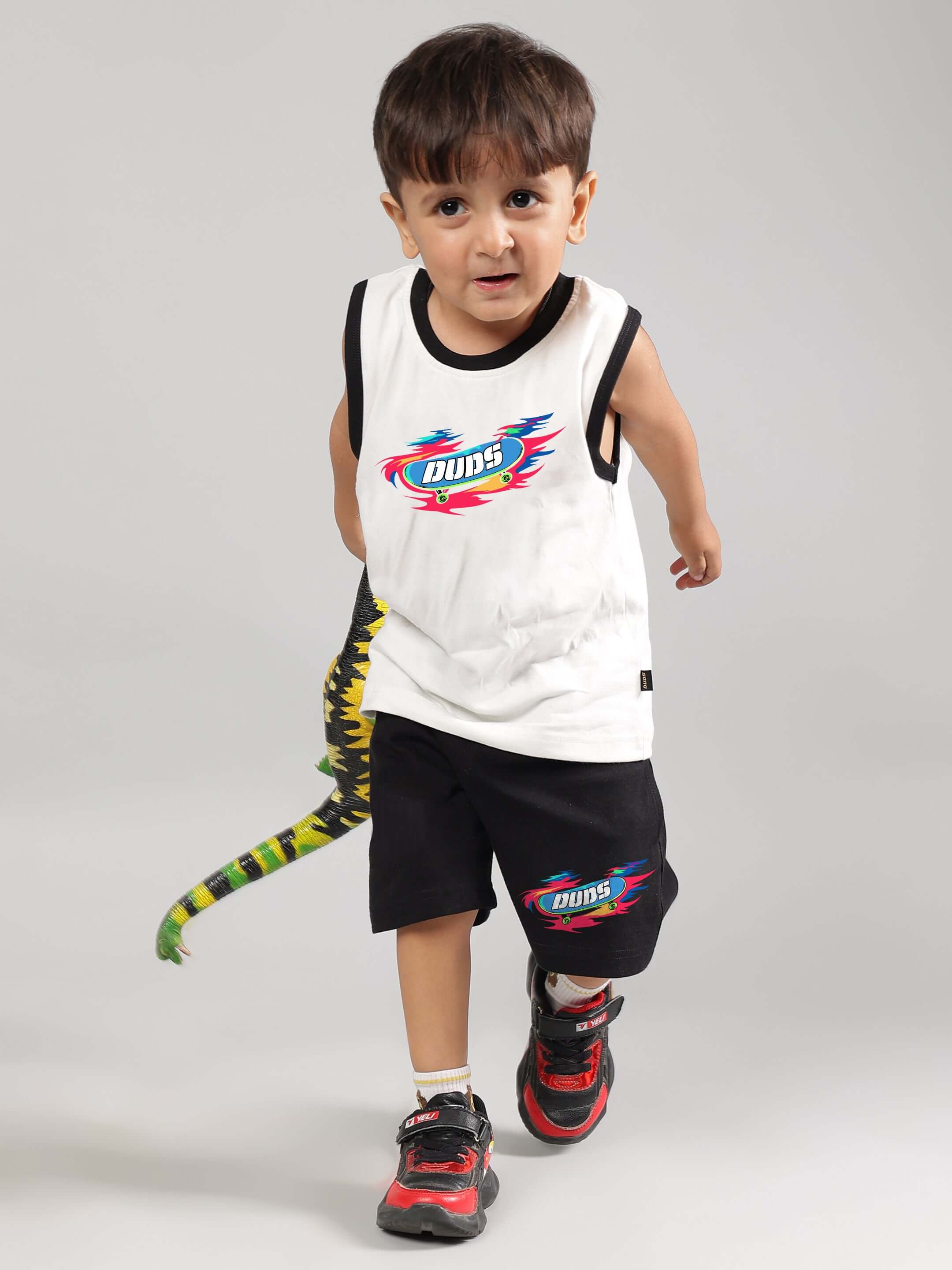 Child wearing DUDS off-white and black Alien Summer Co-Ord for boys and girls, featuring colorful logo and dinosaur tail accessory.