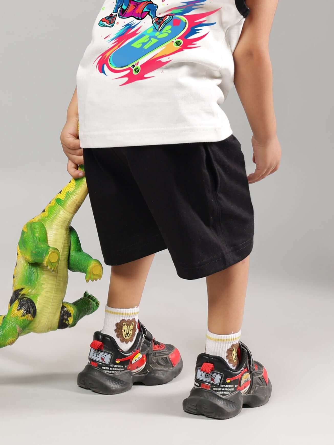 Child wearing ALIEN shorts in black, featuring a playful dinosaur toy, showcasing DUDS's custom fit option for a trendy look.