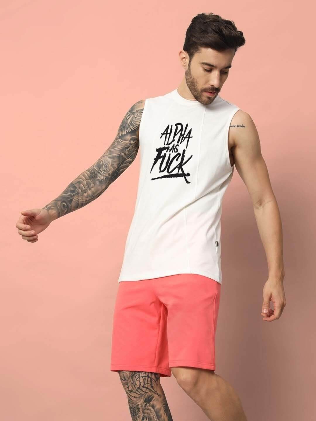 Man wearing ALPHA AS FUCK off-white gym t-shirt with pink shorts, showcasing casual fitness style.